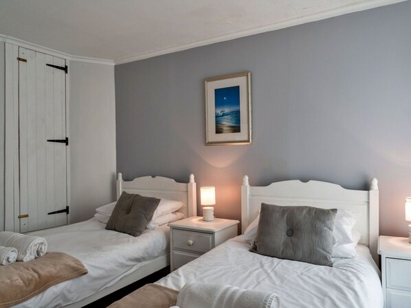A hotel room with two single beds, a nightstand with a lamp, a framed picture on the wall, and a wardrobe with a sliding door.
