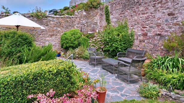 Eine Steinsäule mit Gartenanlage, die Kübelpflanzen, eine Bank und Gartenmöbel zeigt.