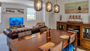 A modern living room with a large wooden dining table, leather sofas, and pendant lighting. - Wonderful  villa for 4 guests with WIFI and terrace (Cawsand)