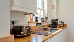 A modern kitchen with a black toaster, copper wire baskets, a coffee maker, and a window with a view. - Wonderful  villa for 4 guests with WIFI and terrace (Cawsand)
