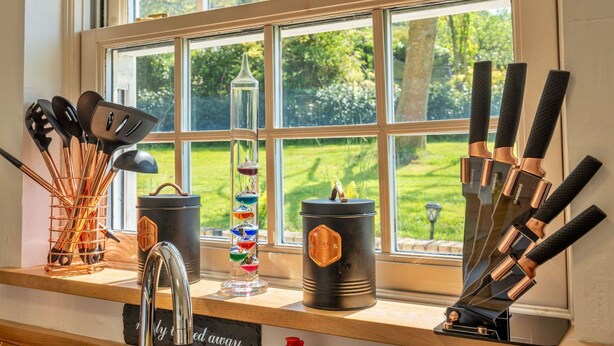 A kitchen counter with various utensils, a coffee maker, and a window with a view of a garden. - Wonderful  villa for 4 guests with WIFI and terrace (Cawsand)