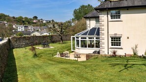 A house with a conservatory, stone wall, and a grassy yard with outdoor furniture. - Wonderful  villa for 4 guests with WIFI and terrace (Cawsand)
