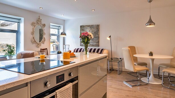 A modern kitchen with a central island, built-in oven, and a dining area with a round table and chairs. - Beautiful  villa for 6 guests with WIFI and terrace (Saltash)
