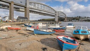 A waterfront with several boats docked on the shore, a large bridge in the background, and a building with a sign. - Beautiful  villa for 6 guests with WIFI and terrace (Saltash)