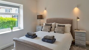 A bedroom with a large bed, bedside lamps, a nightstand, and a window with a view of greenery. - Beautiful  villa for 6 guests with WIFI and terrace (Saltash)