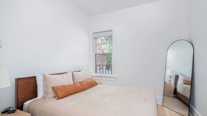 Un dormitorio con cama, mesita de noche, espejo, ventana y vistas al exterior.