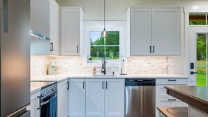 A modern kitchen with white cabinets, stainless steel appliances, and a window providing natural light. - Canandaigua | CMAC | Fire Pit | Hot Tub | Sauna (Canandaigua)