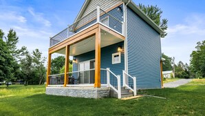 A two-story house with a balcony, a porch, and a stone foundation. - Canandaigua | CMAC | Fire Pit | Hot Tub | Sauna (Canandaigua)