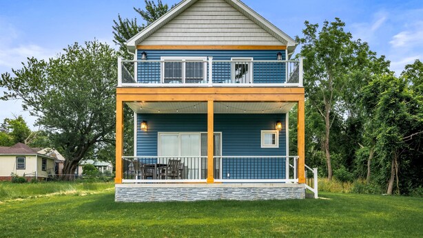 A two-story house with a balcony, a stone foundation, and a grassy yard. - Canandaigua | CMAC | Fire Pit | Hot Tub | Sauna (Canandaigua)
