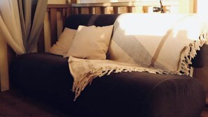 A dark brown sofa with a white and gray blanket, positioned against a wooden wall with a window and curtains.