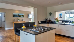 A modern kitchen with a central island, white cabinetry, and a dining area with black chairs. - Wonderful  villa for 12 guests with WIFI, hot tub, terrace and pets allowed (Burnham-on-sea)
