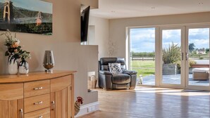 A spacious living room with a wooden cabinet, a leather sofa, and a large window offering a view of the outdoors. - Wonderful  villa for 12 guests with WIFI, hot tub, terrace and pets allowed (Burnham-on-sea)