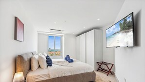 Ein modernes Schlafzimmer mit einem großen Bett, einem an der Wand montierten Fernseher und einem Fenster mit Blick auf den Strand.