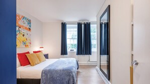 Une chambre à coucher avec un lit, une table de chevet, une fenêtre avec des rideaux et un grand miroir.