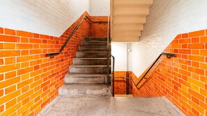 Un escalier aux murs en briques orange et au sol en béton, menant à une porte située en haut.