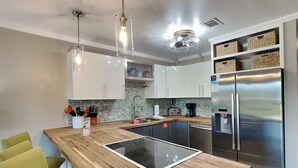 A modern kitchen with white cabinets, a stainless steel refrigerator, a built-in island with a glass top, and pendant lighting. - Coconut’s Beach House | 2BD/1.5BA | Steps to Beach,  Lake View + Outdoor Shower (Pensacola Beach)