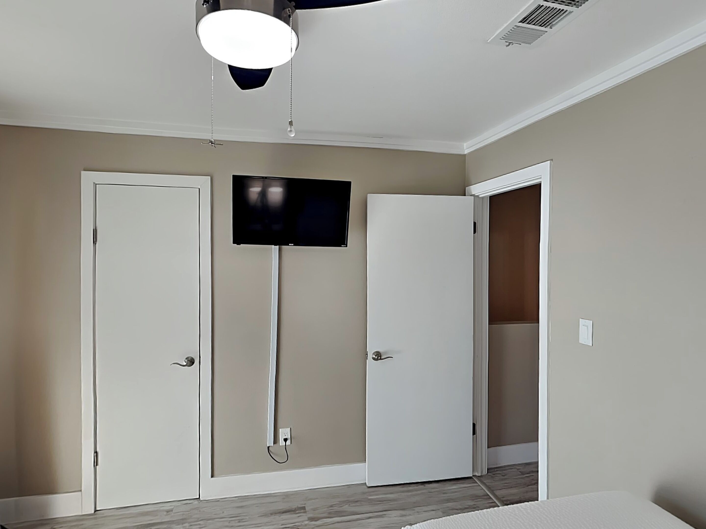 A bedroom with a bed, a TV mounted on the wall, and two doors.
