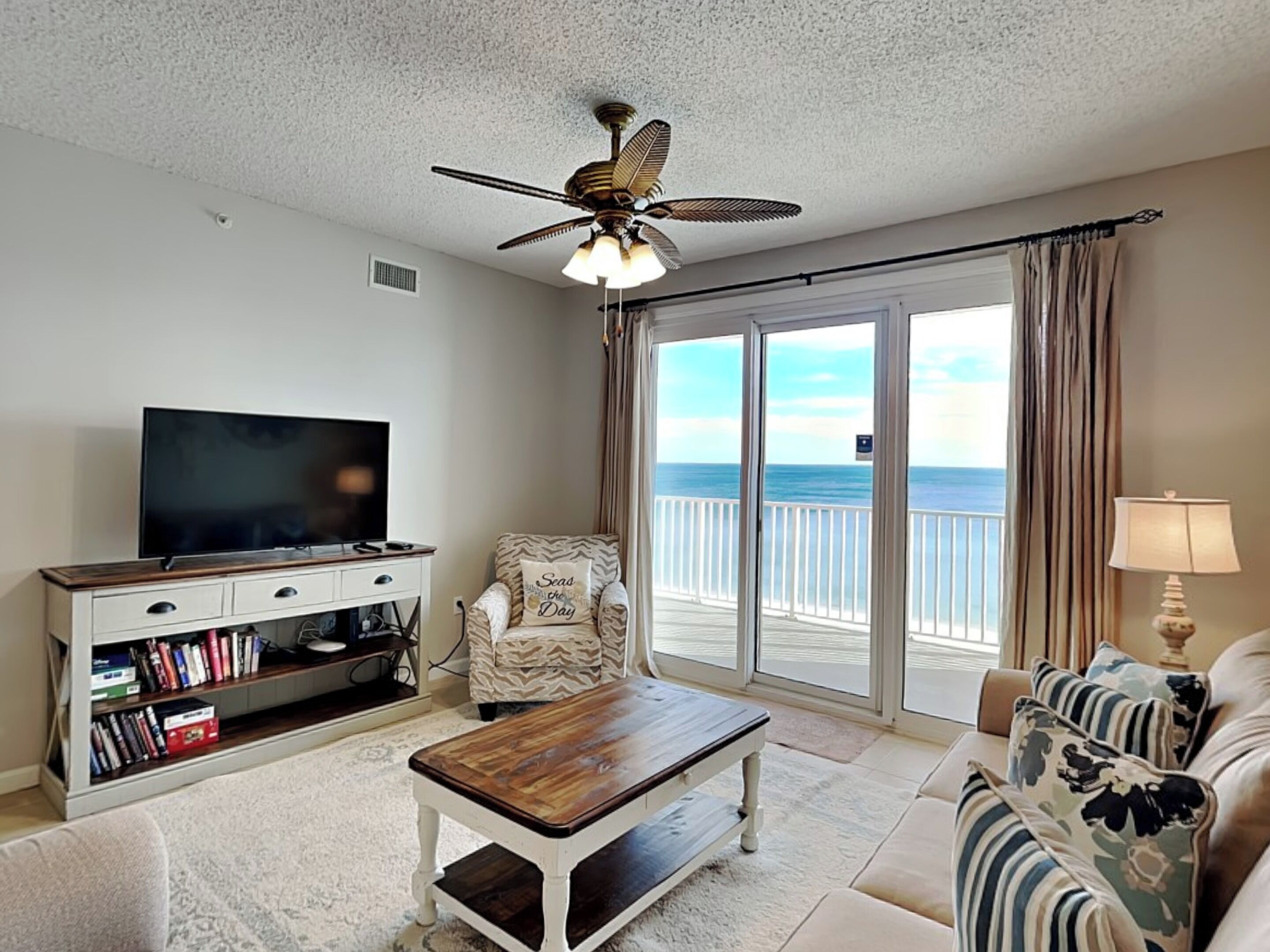 A living room with a TV, bookshelf, and a view of the ocean through large sliding doors.