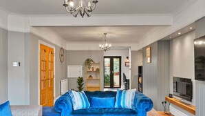 Un salon avec un canapé bleu, un canapé gris, un lustre et un téléviseur posé sur un meuble en bois.