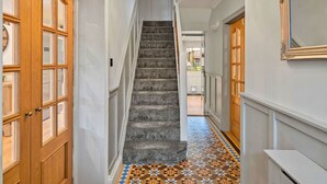 Un couloir avec un escalier recouvert de moquette, des portes en bois et un sol à motifs.