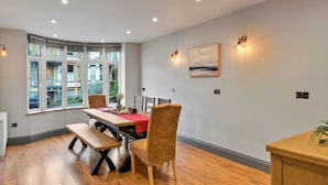 Un coin repas avec une table en bois, des chaises et un banc. Une fenêtre offre une vue sur les bâtiments environnants.