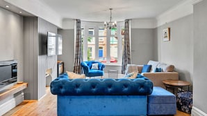 Un salon moderne avec un canapé bleu, un téléviseur et un coin repas comprenant une table et des chaises.