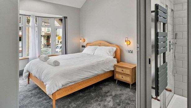 Une chambre dotée d’une lucarne, d’un lit avec du linge de lit blanc, d’une table de chevet, d’une lampe fixée au mur, et d’une salle de bain avec une douche et un radiateur.
