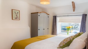 A bedroom with a bed, a wardrobe, a window with curtains, and a picture on the wall.