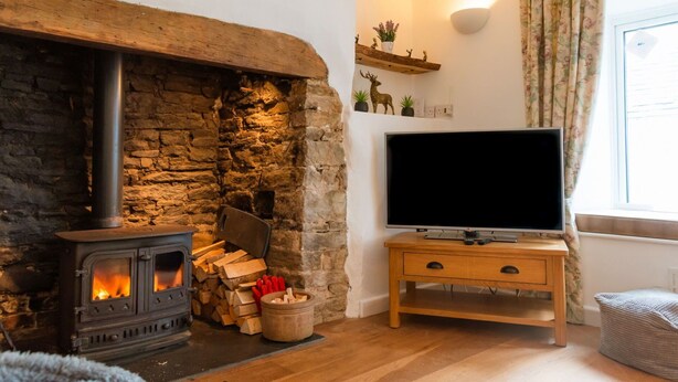 A cozy living room with a stone fireplace, a television on a wooden stand, and a window with curtains.