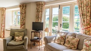 A living room with a sofa, a chair, a TV, and a table with a lamp. - Stunning  villa for 8 guests with WIFI, TV and pets allowed (Minehead)