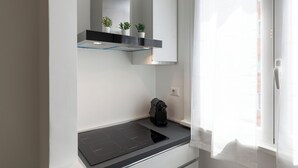 A modern kitchen with a black countertop, a built-in stove, and a small shelf with potted plants. - notaMi - Fiordalisi 1 - Flower District (Milan)