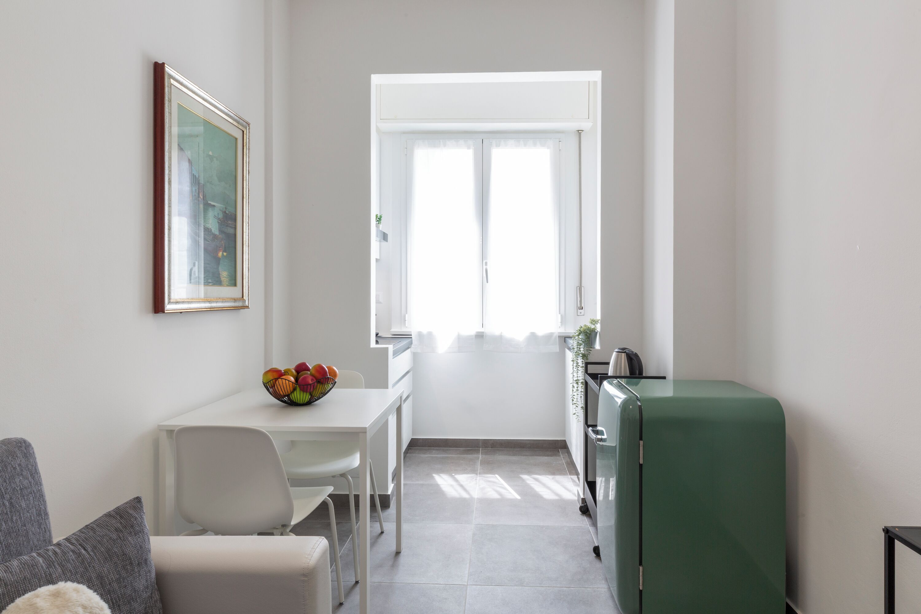Ett kompakt bostadsutrymme med en matplats, ett grönt kylskåp och ett fönster som släpper in naturligt ljus.