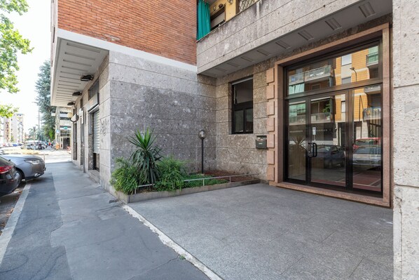 Un bâtiment doté d’une façade en pierre, d’une entrée en verre et d’un petit jardin.
