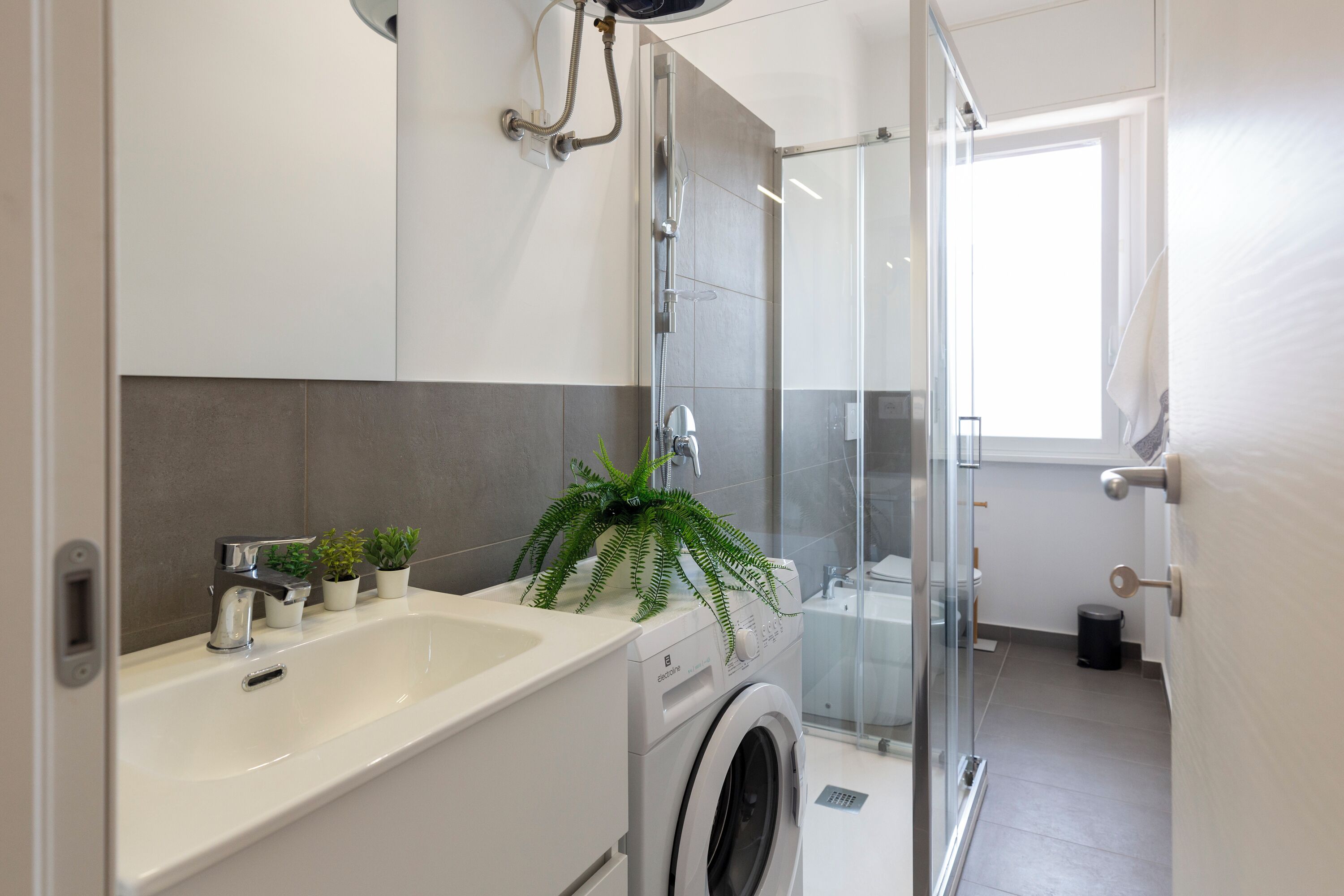 A modern bathroom with a built-in washing machine, a sink, and a shower area.