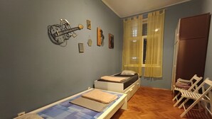 Une chambre avec un lit simple, une petite table, une chaise, une décoration murale représentant un vélo et une fenêtre avec des rideaux.