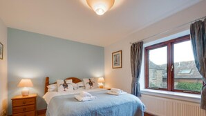 A bedroom with a bed, bedside tables, a window with curtains, and a radiator.