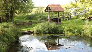 A rustic wooden structure with a sloped roof, situated beside a calm water body with reflections.
