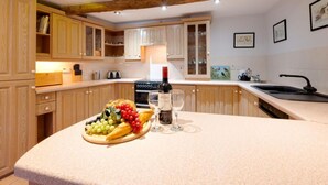 A kitchen with wooden cabinets, a central island with a fruit platter and wine glasses, and a built-in oven.