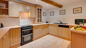 A kitchen with wooden cabinets, a black stove, a sink, and a countertop with fruits and a bottle.
