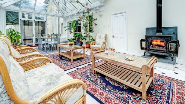 A conservatory with a glass ceiling, wicker furniture, a wooden table, and a black wood-burning stove. - Wonderful  villa for 14 guests with WIFI and pets allowed (Dartmouth)