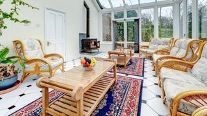 A sunroom with a glass ceiling, wicker furniture, a wooden table, and a fireplace. - Wonderful  villa for 14 guests with WIFI and pets allowed (Dartmouth)