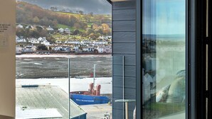 A modern room with a large window overlooking a coastal town, a view of the sea, and a ship docked nearby.