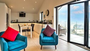A modern living room with two blue armchairs, a dining area, and a kitchen.