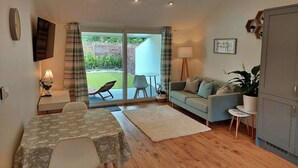 A cozy living room with a sofa, a dining table, and a view of the garden through the sliding glass door. - Stunning  villa for 2 guests with hot tub, WIFI (Kingsteignton)