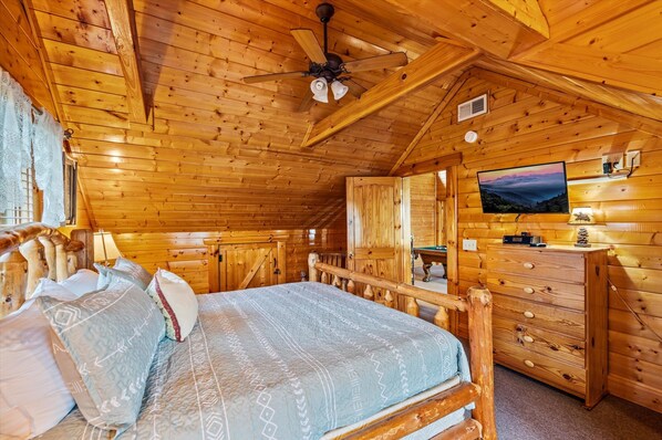 Un dormitorio tipo cabaña de madera con cama, cómoda, televisor y ventilador de techo.