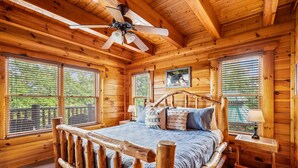 A wooden cabin bedroom with a bed, a ceiling fan, and large windows.
