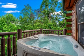 Ein Whirlpool auf einer Holzterrasse mit Blick auf üppige, grüne Bäume.