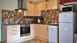A compact kitchen with a Bosch oven, a microwave, and a dishwasher. There are wooden cabinets and a tiled backsplash.