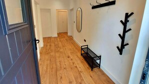 A hallway with wooden flooring, a bench, a mirror, and wall-mounted hooks.