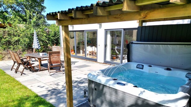 A hot tub under a pergola, a patio table, and chairs.